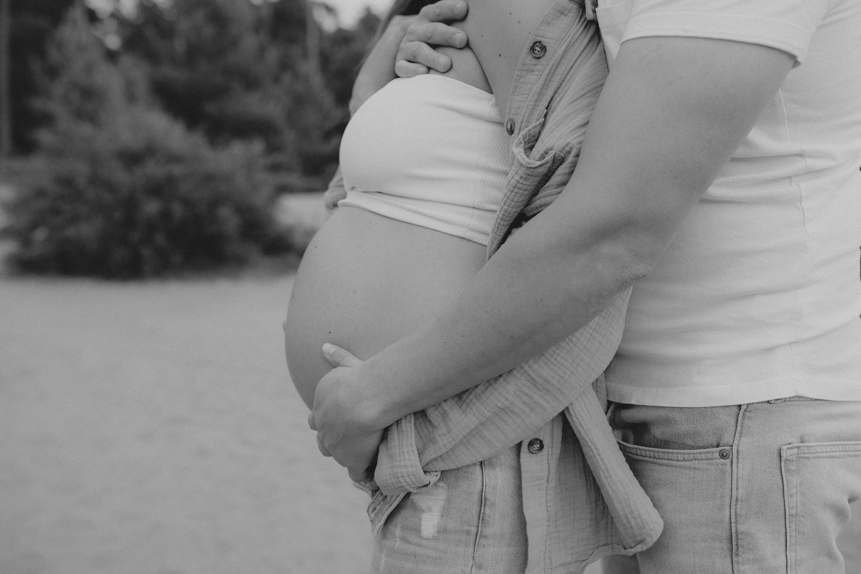 Detailaufnahme im Profil: Der Mann legt seinen Arm liebevoll um den Babybauch seiner Partnerin